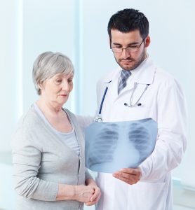 Senior patient looking attentively at x-ray held by radiologist in hospital